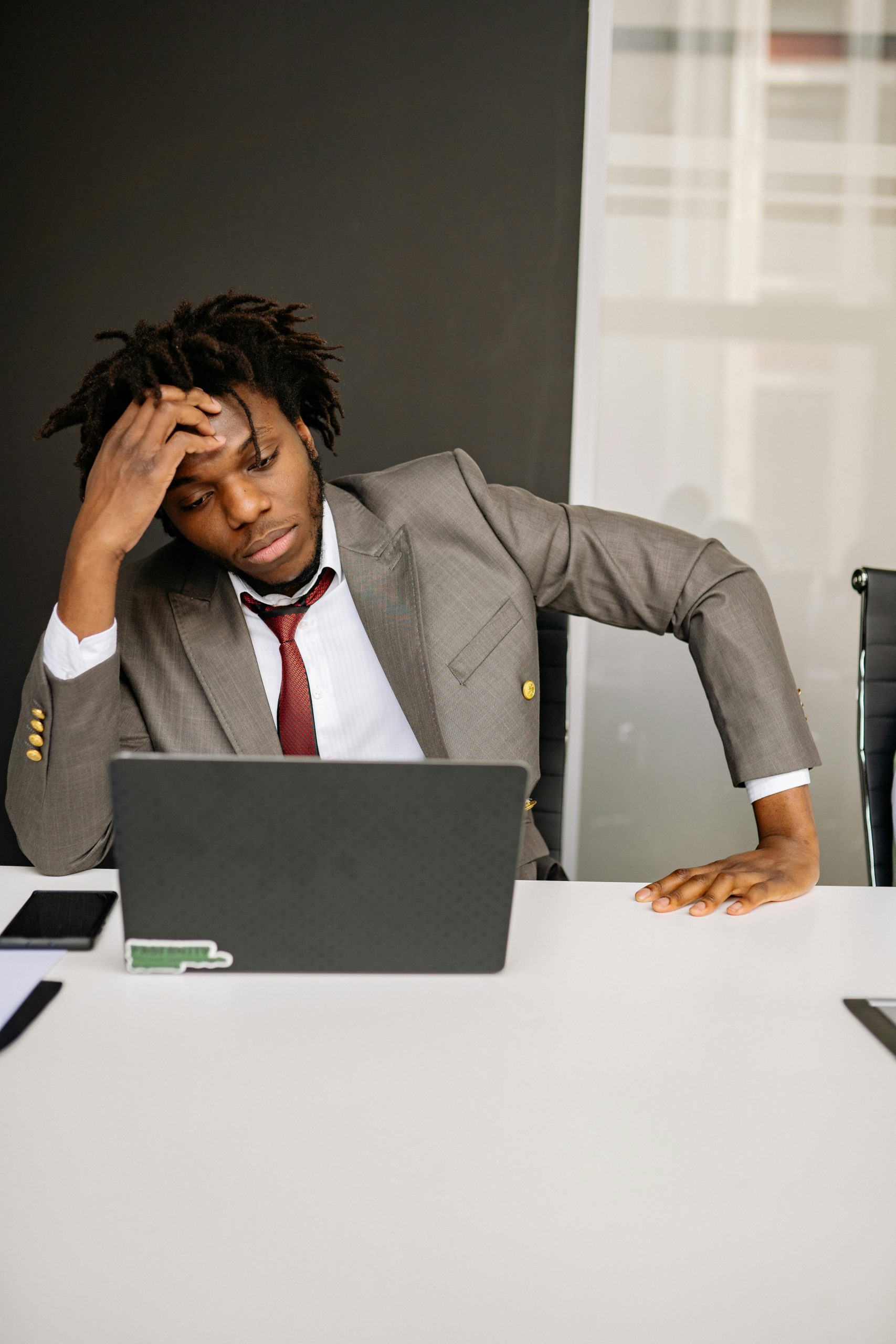 An adult man looking stressed while working on a laptop in an office.